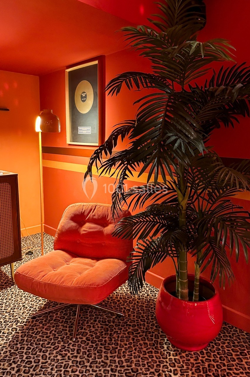 Fauteuil orange devant un mur rouge décoré d'un disque d'or, avec une plante en pot et un sol à motif léopard.