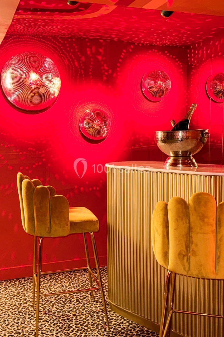 Bar avec tabourets en velours jaune, mur rouge décoré de luminaires circulaires et sol à motif léopard.