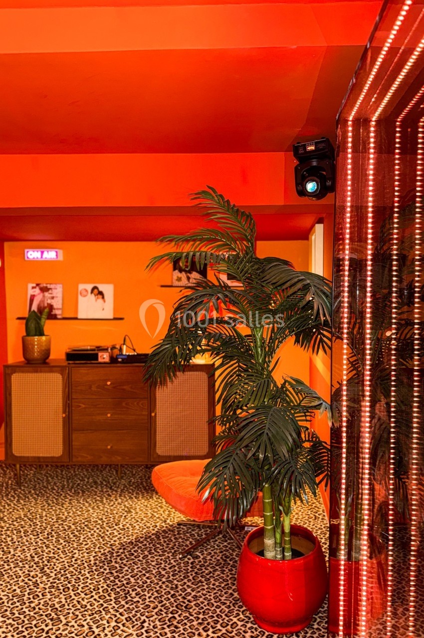 Intérieur rétro avec murs orange, mobilier vintage, plante en pot rouge et sol à motif léopard.