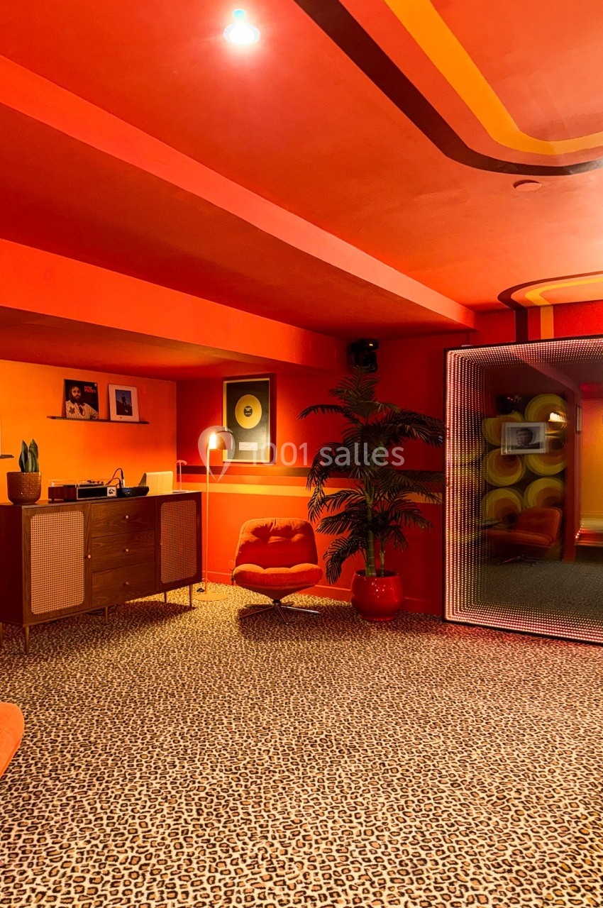 Salle rétro avec tapis léopard, mobilier vintage, plantes, éclairage tamisé et décorations murales colorées.