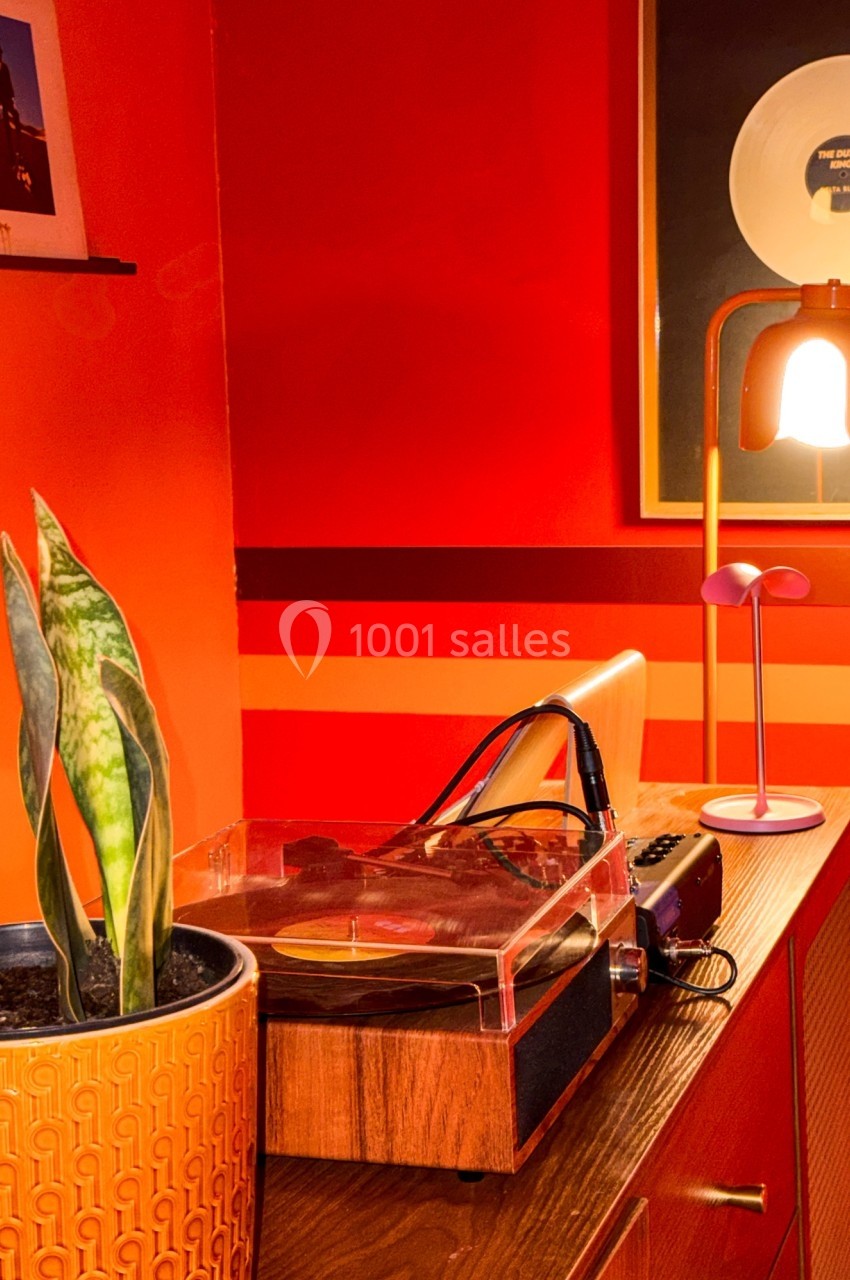 Platine vinyle sur un meuble en bois, plante en pot et lampes dans une pièce aux tons rouges et orange.