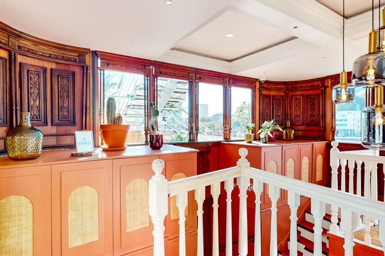 Intérieur lumineux avec boiseries sculptées, plantes en pot et suspensions en verre, vue sur l'extérieur par de grandes…