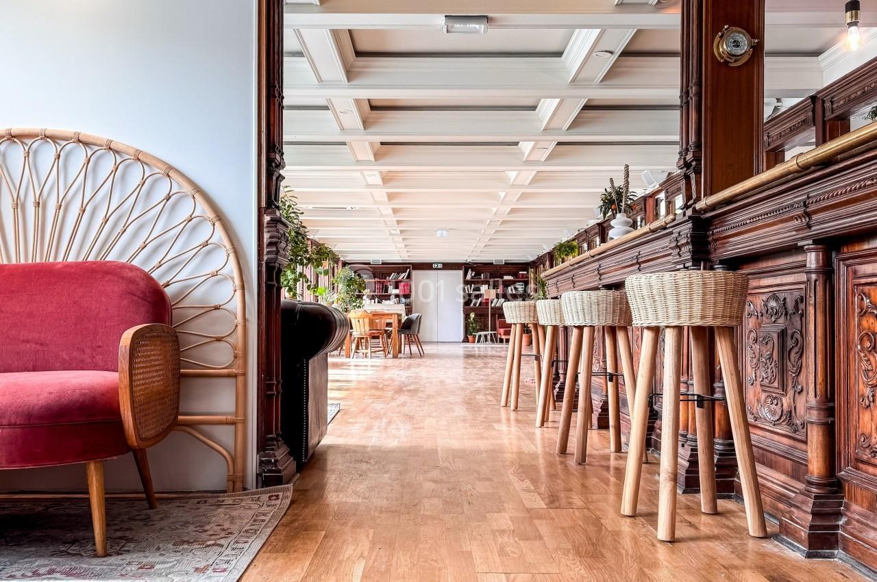 Espace intérieur lumineux avec un comptoir en bois sculpté, tabourets en rotin et fauteuil rouge près d'une table basse.