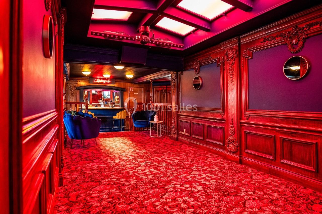 Couloir richement décoré avec moquette rouge, murs en bois sculpté et vue sur un espace lounge éclairé.