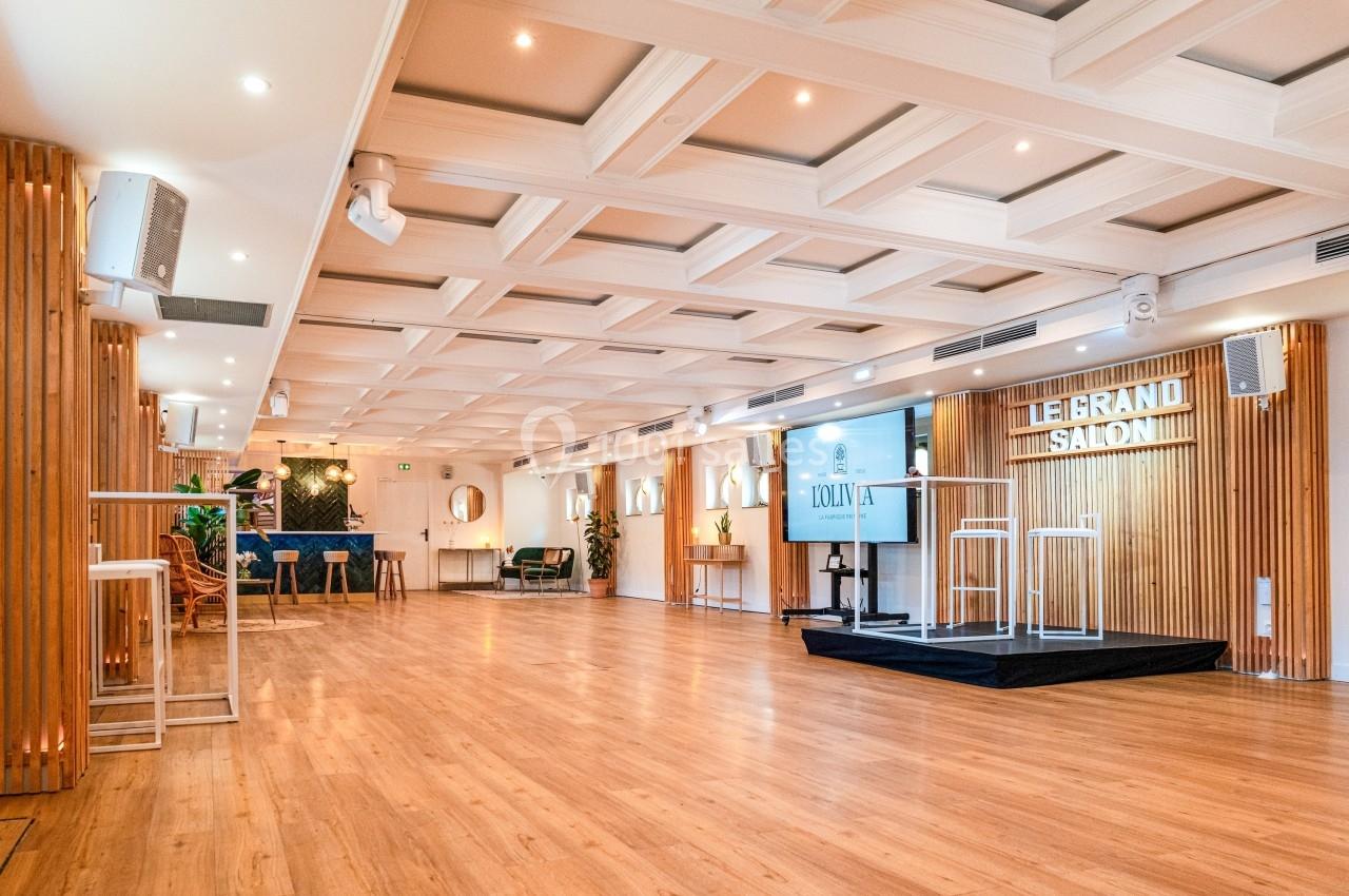 Salle lumineuse avec parquet, plafond à caissons, estrade, mobilier moderne et éclairage intégré.