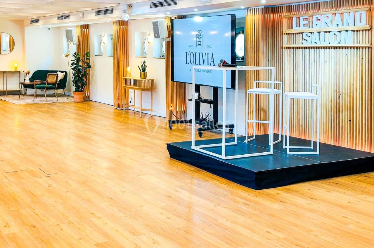 Salle lumineuse avec parquet, estrade équipée de chaises hautes et écran, décorée de panneaux en bois et plantes.