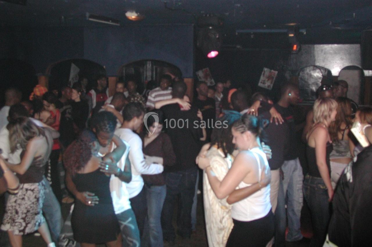 Personnes dansant en couple dans une salle sombre, ambiance festive avec plusieurs groupes rapprochés.
