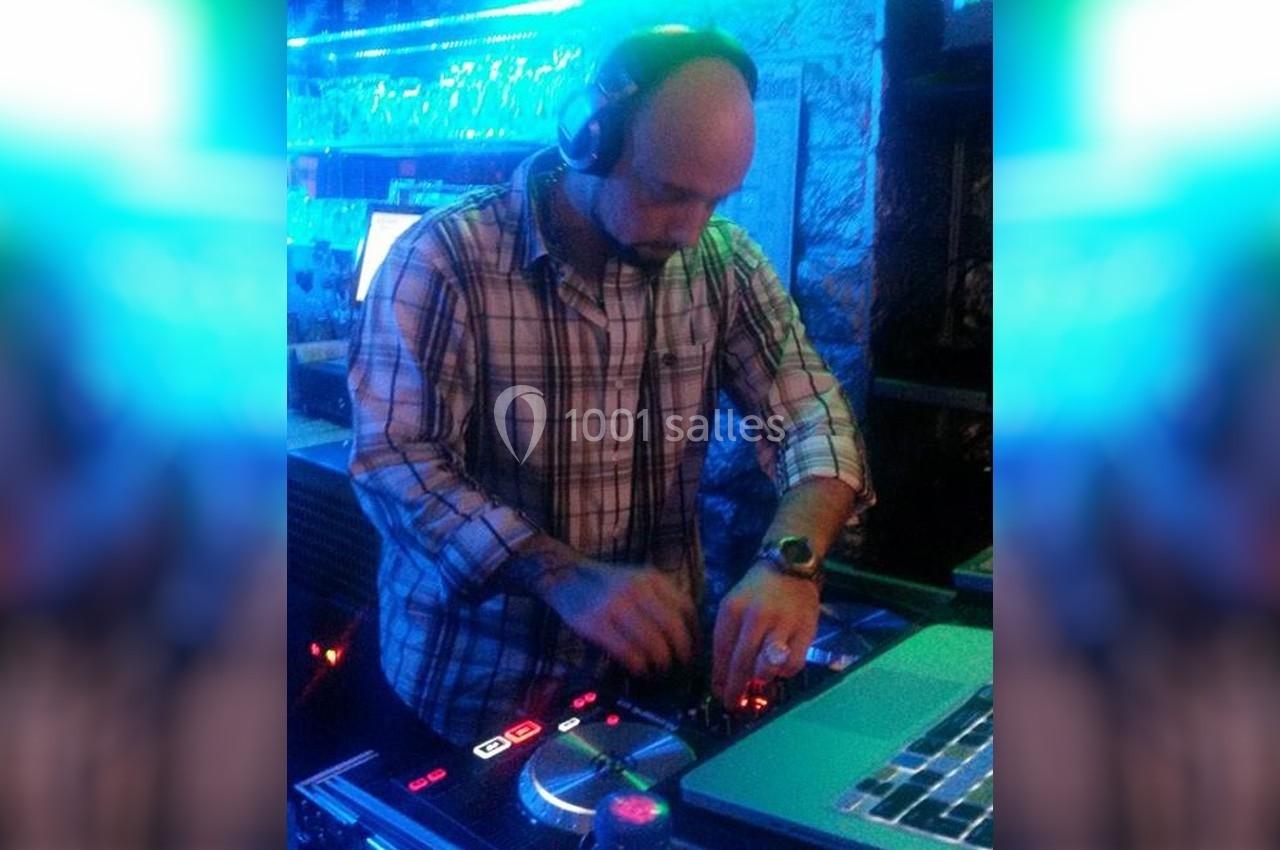 Un DJ en chemise à carreaux mixe de la musique sur une console dans un environnement éclairé en bleu.