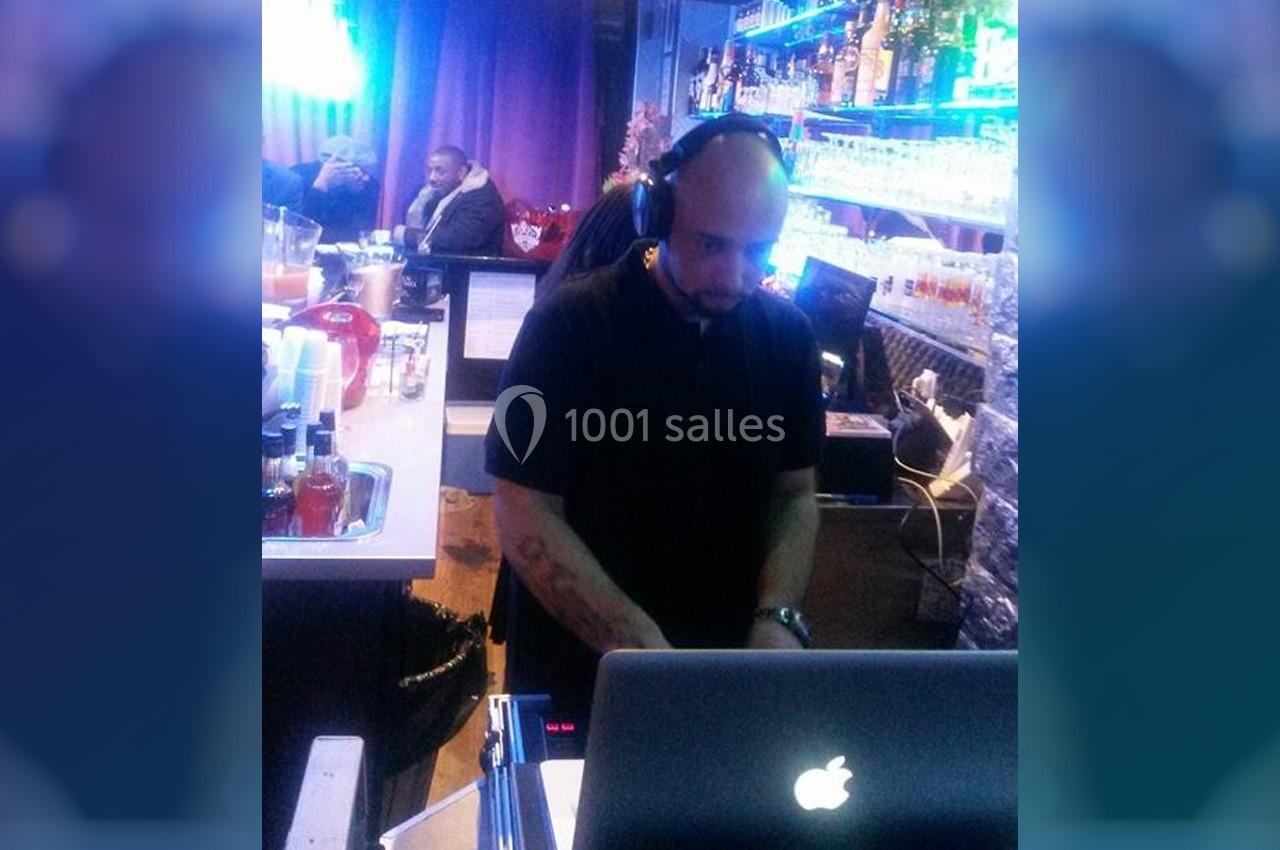 Un DJ mixant de la musique derrière un ordinateur portable dans un bar éclairé par des lumières bleues.