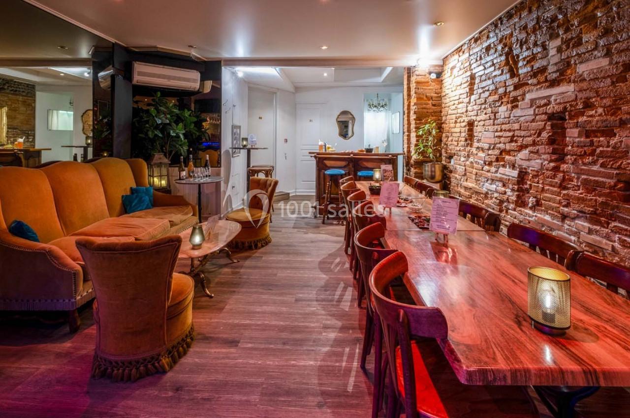 Salle chaleureuse avec murs en briques, table en bois, fauteuils confortables et éclairage tamisé.