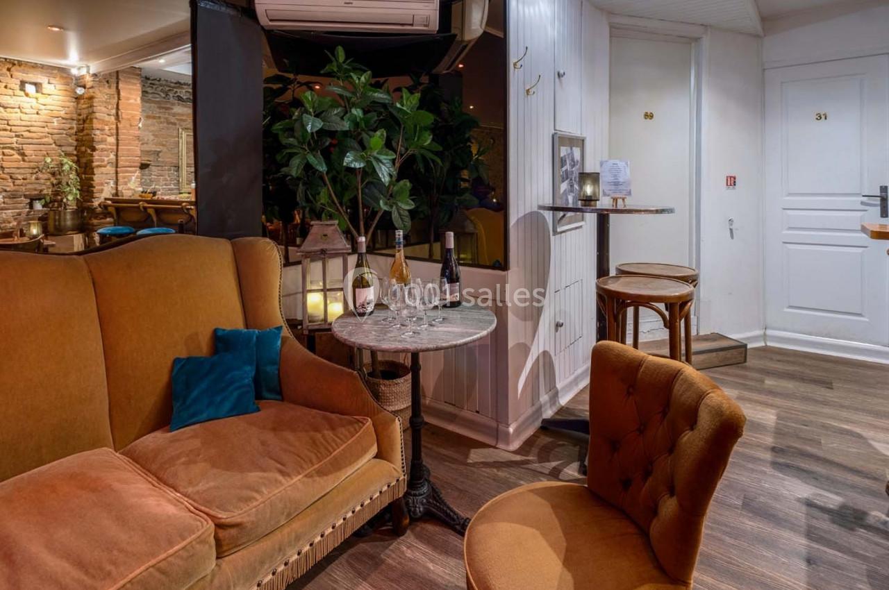 Salon cosy avec fauteuils en velours, table ronde, plantes et éclairage chaleureux dans un espace intérieur.