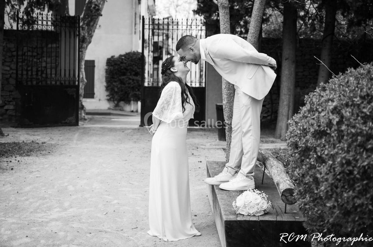 Un couple de mariés échange un moment complice dans un jardin, l'homme debout sur une plateforme embrasse la femme.