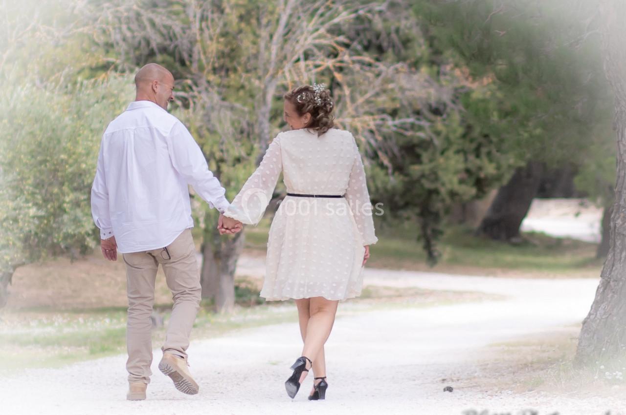 Un couple marche main dans la main sur un chemin bordé d'arbres, dans un cadre naturel et paisible.