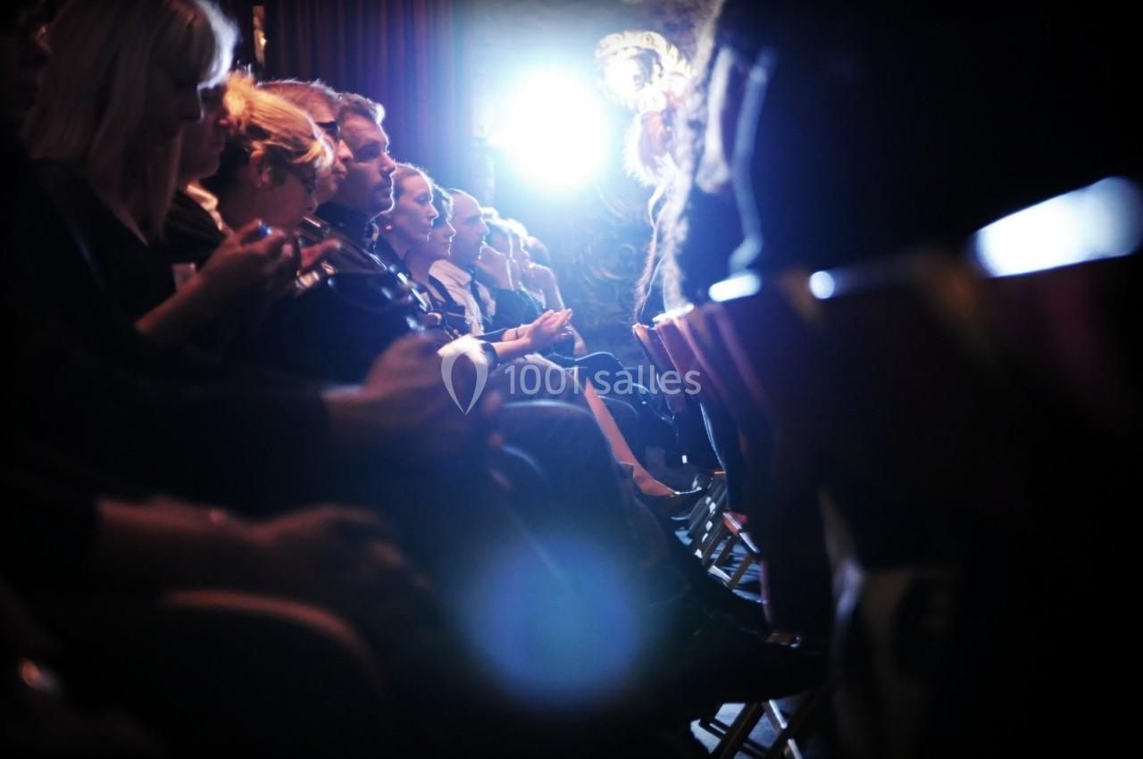 Des personnes assises en rangées dans une salle sombre, éclairées par une lumière vive à l'arrière-plan.