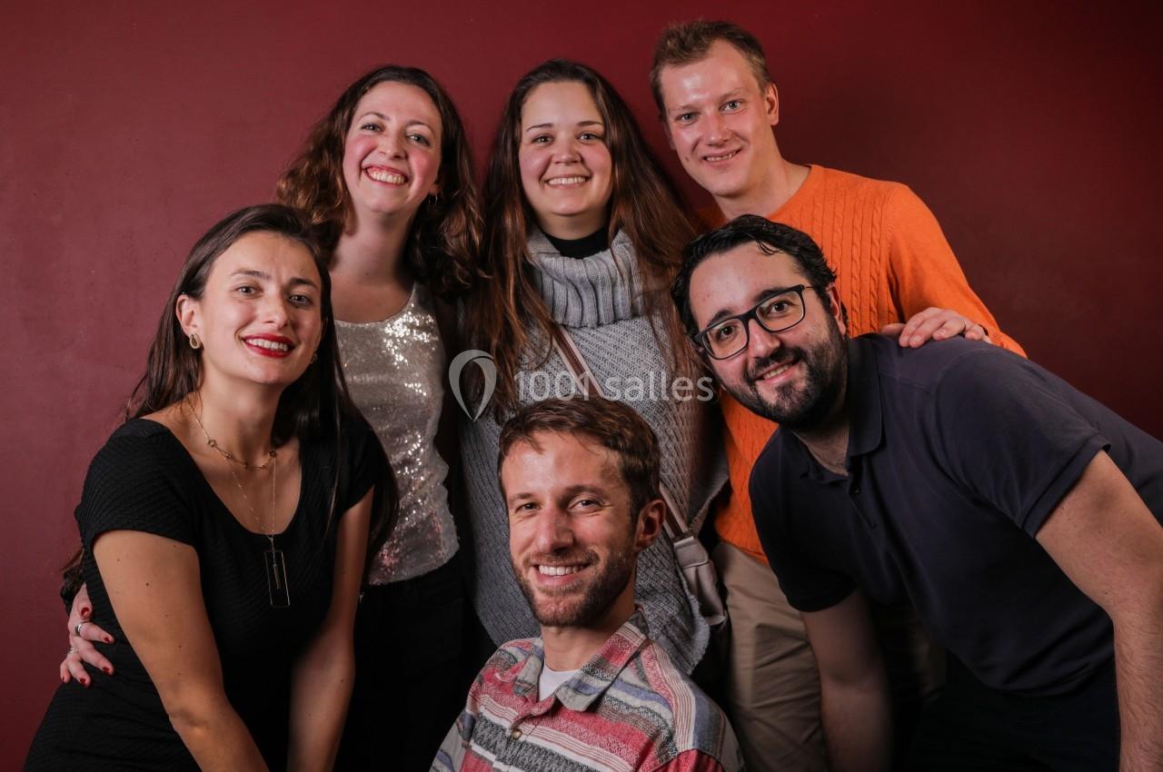 Un groupe de six personnes souriantes posant devant un mur rouge.