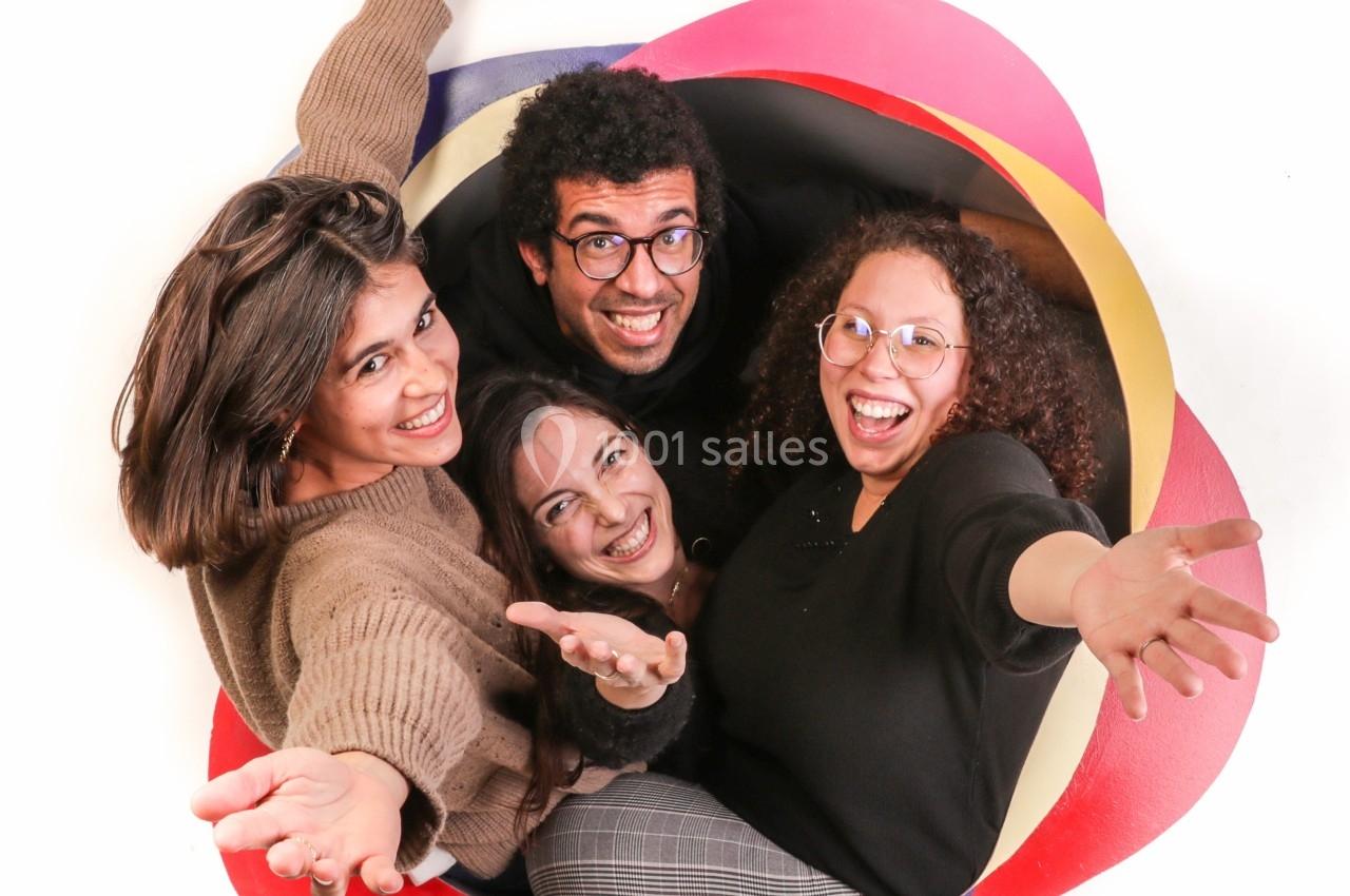 Quatre personnes souriantes posent ensemble à travers une ouverture colorée, bras tendus vers l'objectif.