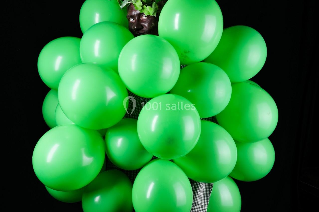 Personne déguisée en grappe de raisin avec des ballons verts et des feuilles, sur fond noir.
