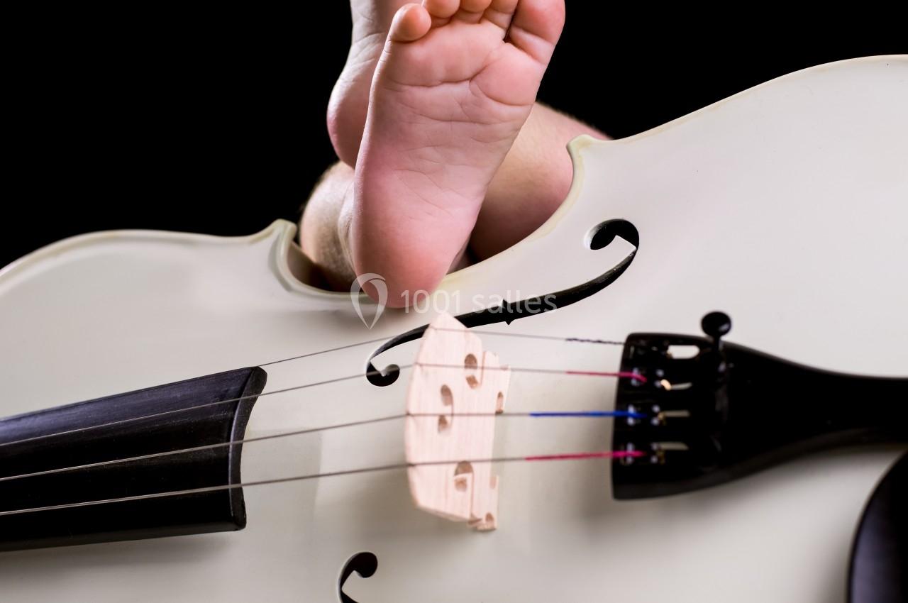 Pieds d'un bébé posés sur un violoncelle blanc, avec un fond noir et une texture de fourrure blanche au sol.