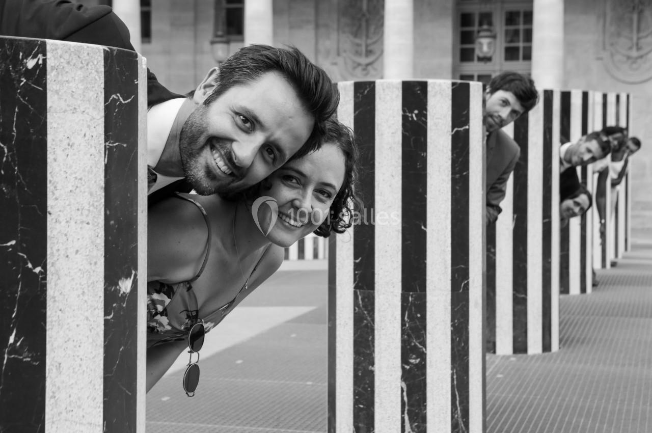 Des personnes souriantes posent derrière des colonnes rayées en noir et blanc dans un espace extérieur.