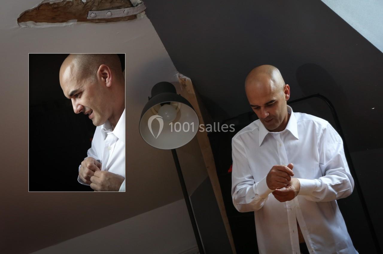 Un homme ajuste les manches de sa chemise blanche dans une pièce éclairée par une lampe sur pied.