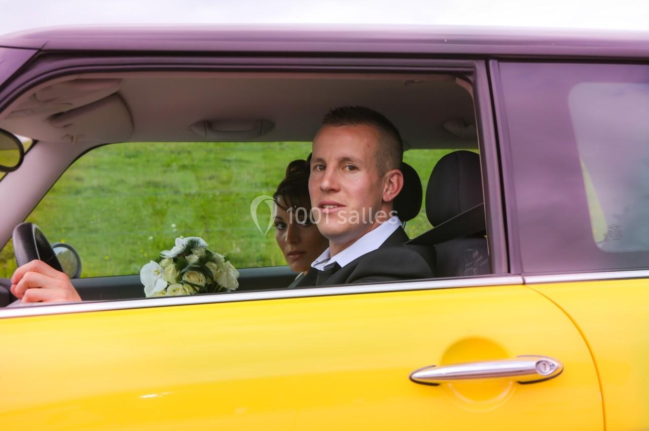 Un couple assis dans une voiture jaune, l'homme au volant et la femme tenant un bouquet de fleurs.