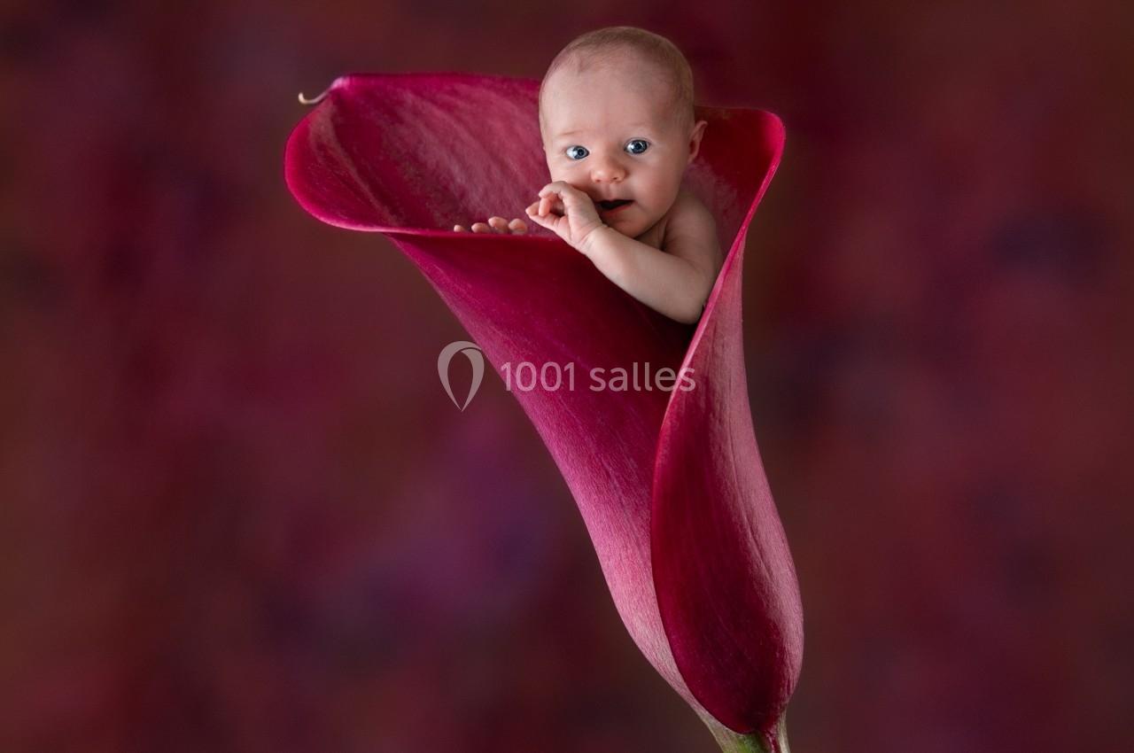 Un bébé émergeant d'une fleur de calla rouge sur un fond flou aux tons chauds.