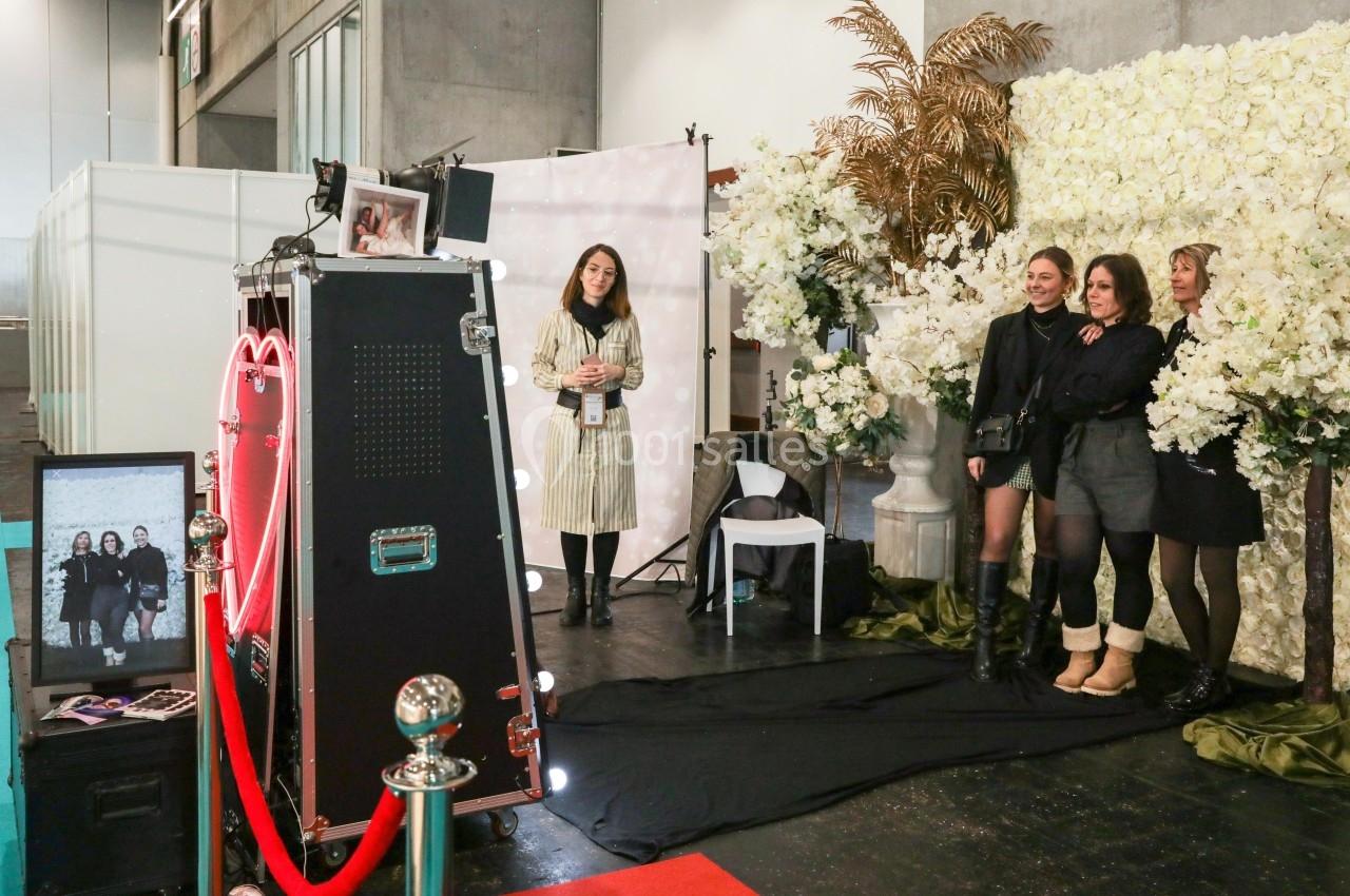 Quatre femmes posent devant un photobooth décoré de fleurs blanches et d'éléments dorés dans un espace intérieur.