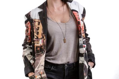 Femme souriante portant un blazer imprimé coloré, un t-shirt gris et un jean, posant devant un fond blanc.