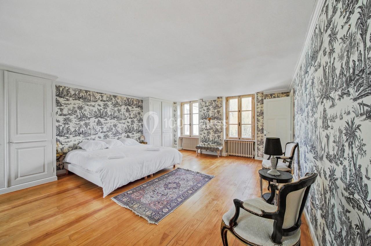 Chambre lumineuse avec lit double, murs ornés de papier peint à motifs, parquet en bois et tapis au sol.