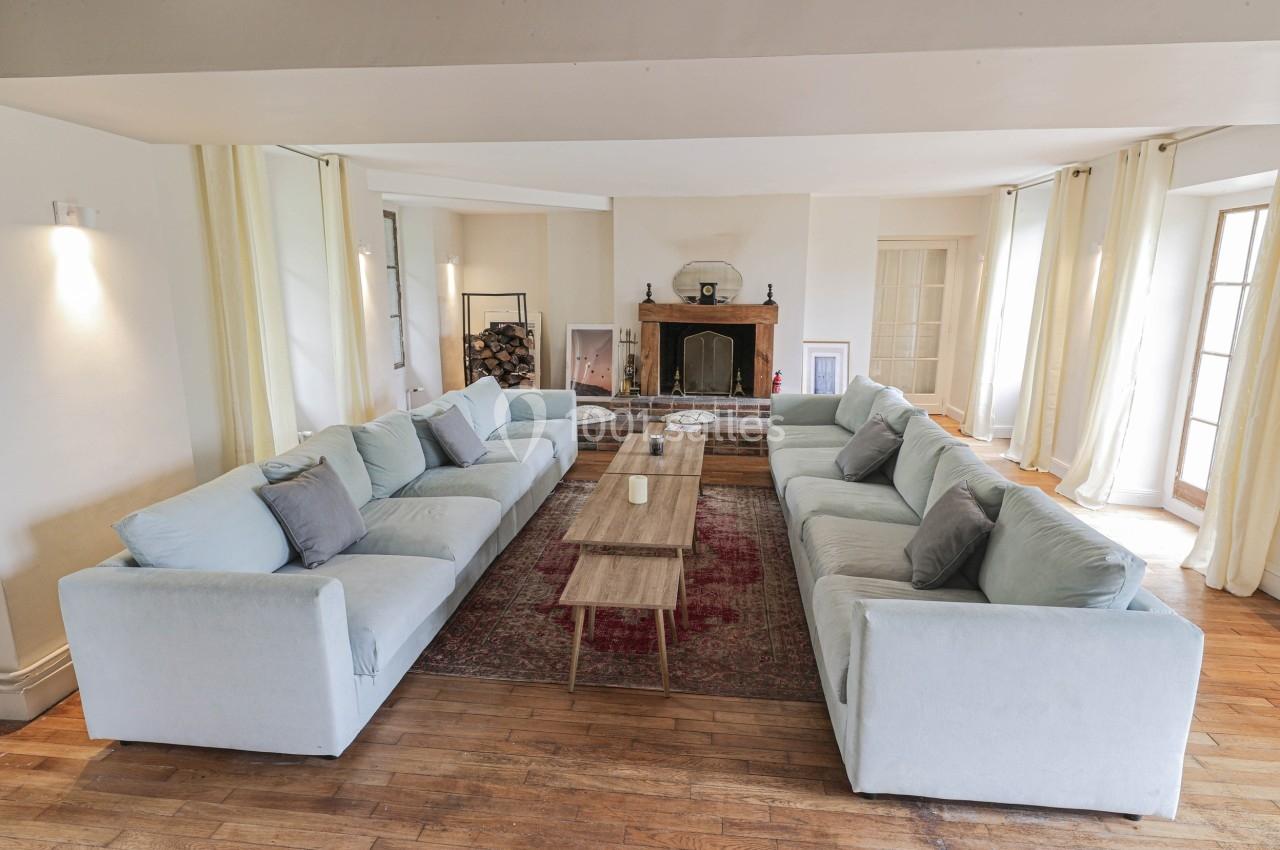 Salon lumineux avec deux grands canapés bleus disposés face à face, table basse en bois et cheminée en arrière-plan.