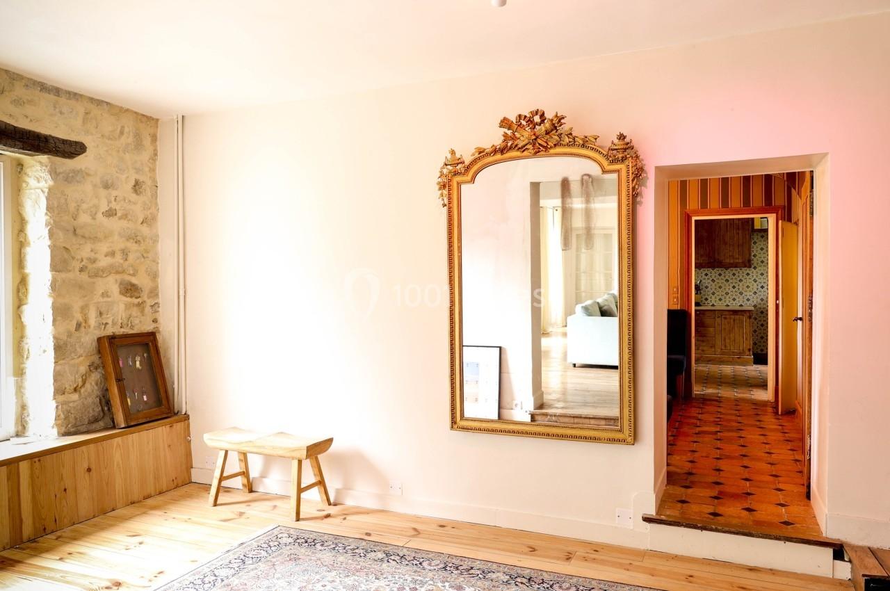 Miroir doré accroché à un mur clair, reflétant une pièce adjacente avec un canapé, dans un intérieur lumineux.