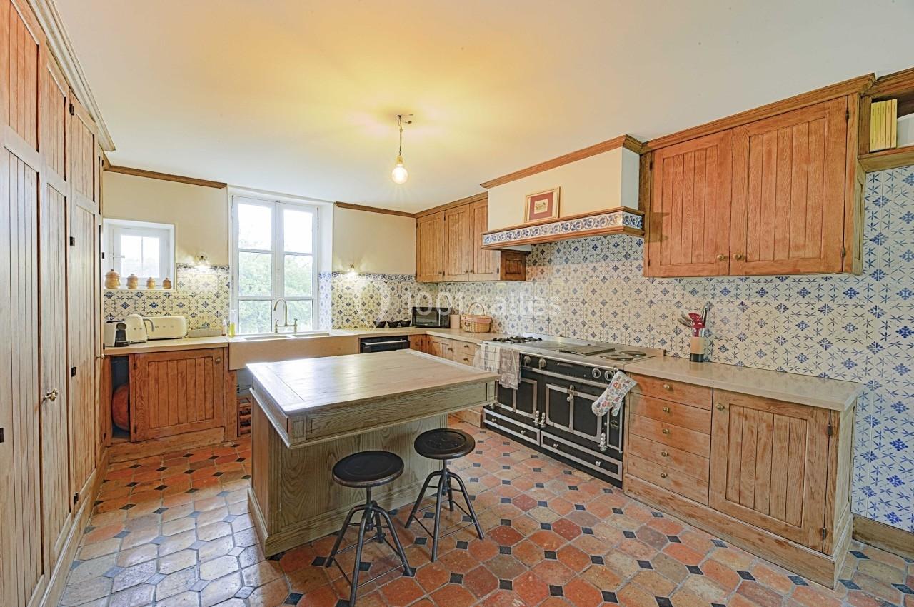 Cuisine rustique avec meubles en bois, îlot central, carrelage ancien et mur décoré de carreaux bleus et blancs.