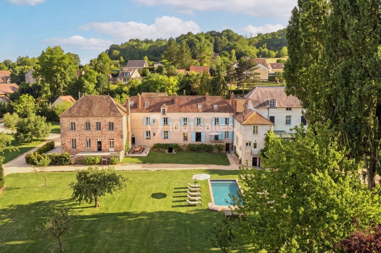 Vue aérienne d'une grande maison de campagne entourée d'un jardin verdoyant avec une piscine et des arbres.