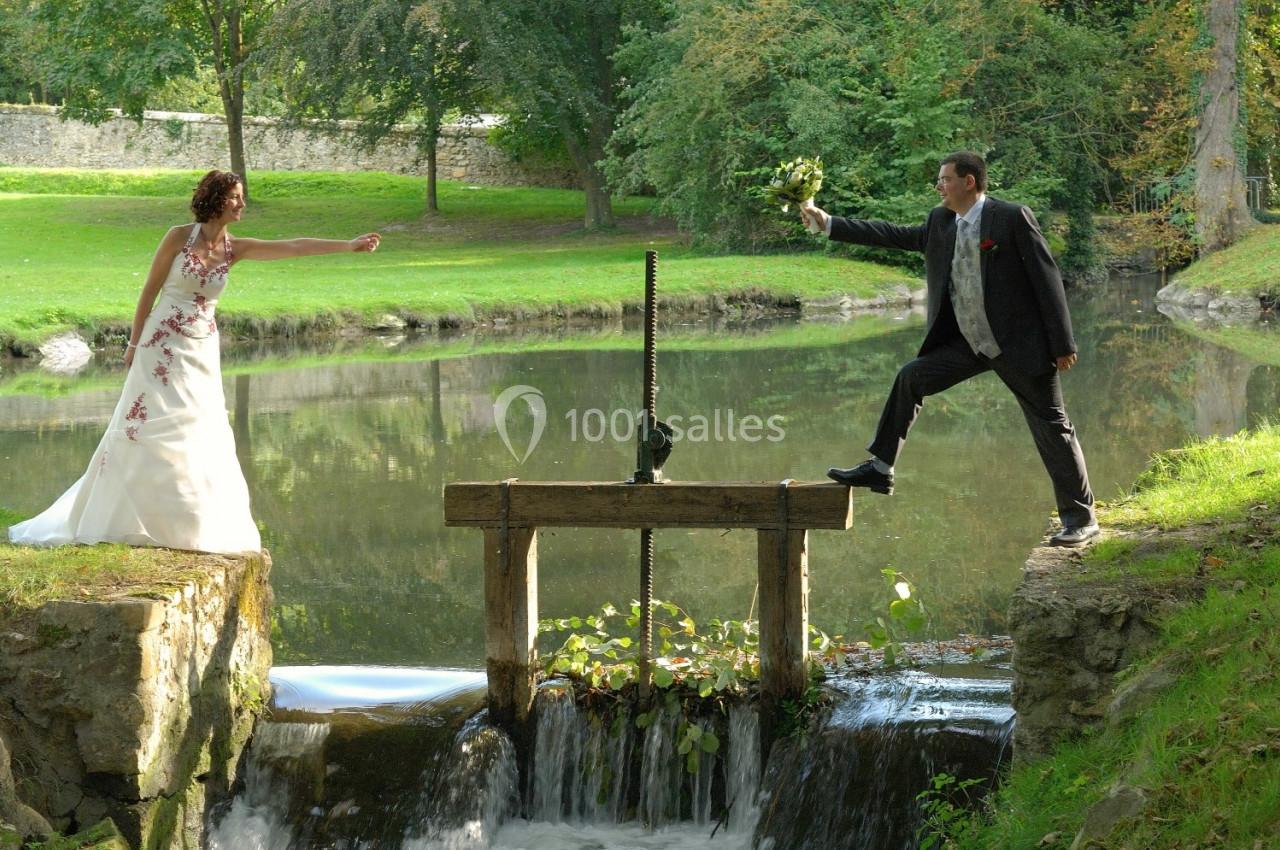 Un couple en tenue de mariage se tient de part et d'autre d'une petite écluse dans un cadre naturel verdoyant.