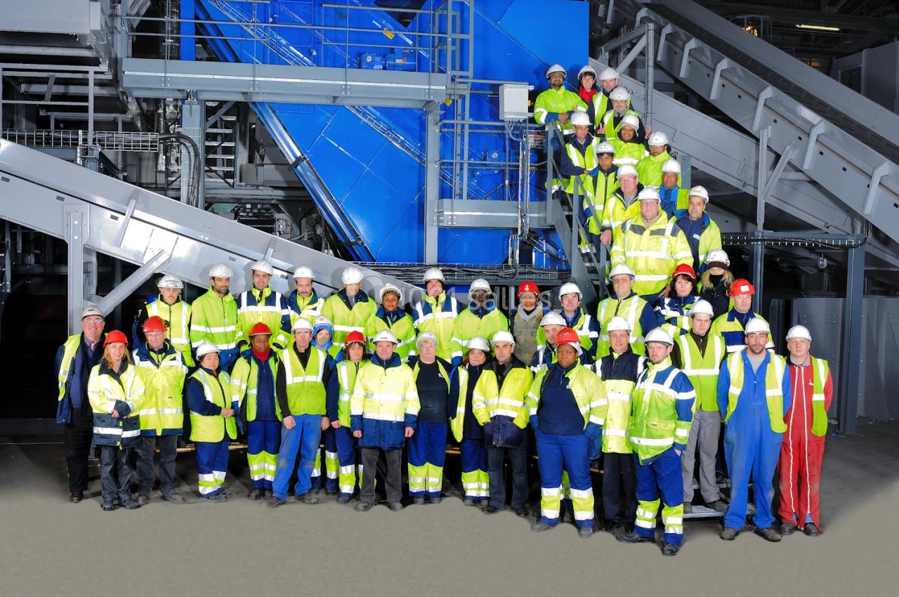 Groupe de travailleurs en tenue de sécurité posant devant des équipements industriels dans un environnement d'usine.
