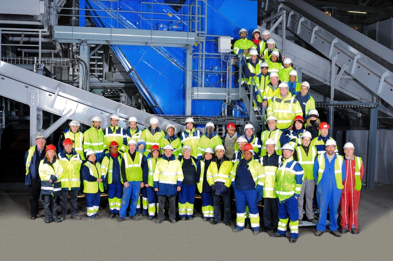 Groupe de travailleurs en tenue de sécurité posant devant des équipements industriels dans un environnement d'usine.