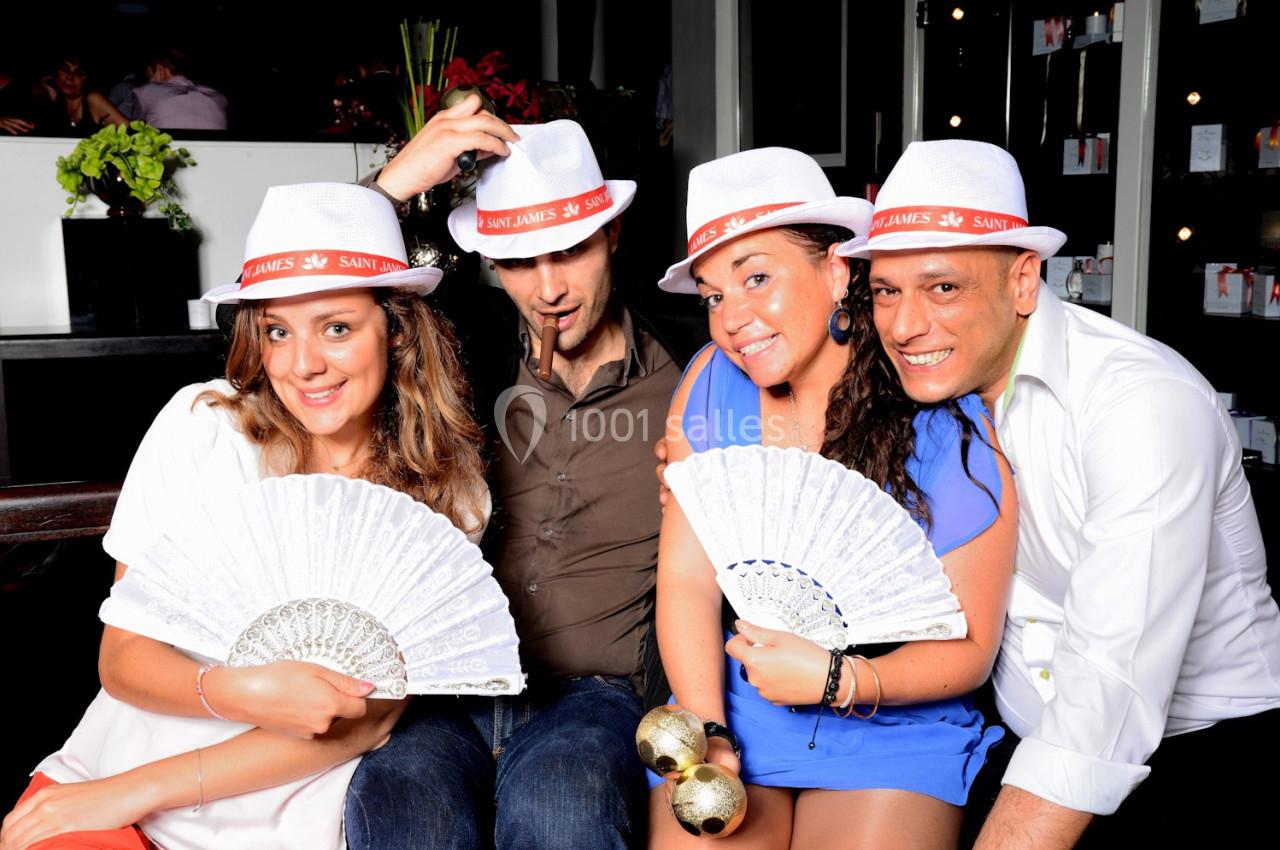 Quatre personnes souriantes portant des chapeaux blancs et tenant des éventails ou des maracas dans un cadre festif.