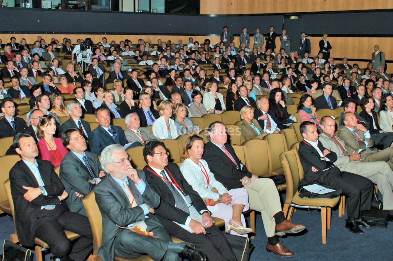 Salle comble avec un public attentif assis sur des rangées de sièges lors d'une conférence ou d'un événement professionnel.