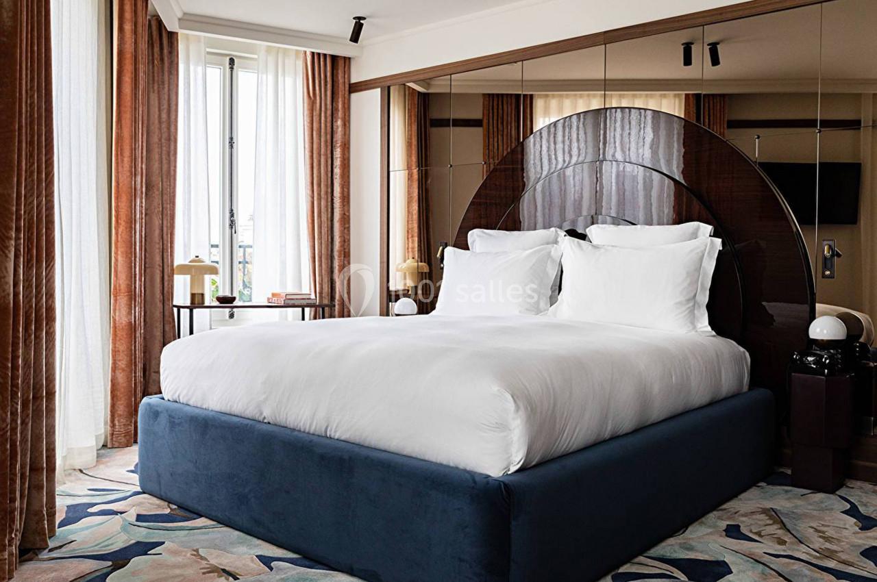 Lit double avec draps blancs dans une chambre élégante, décorée de rideaux marron, miroirs et tapis coloré.