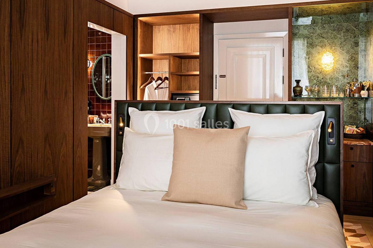 Chambre d'hôtel avec lit double, tête de lit en cuir, placards en bois et salle de bain visible en arrière-plan.