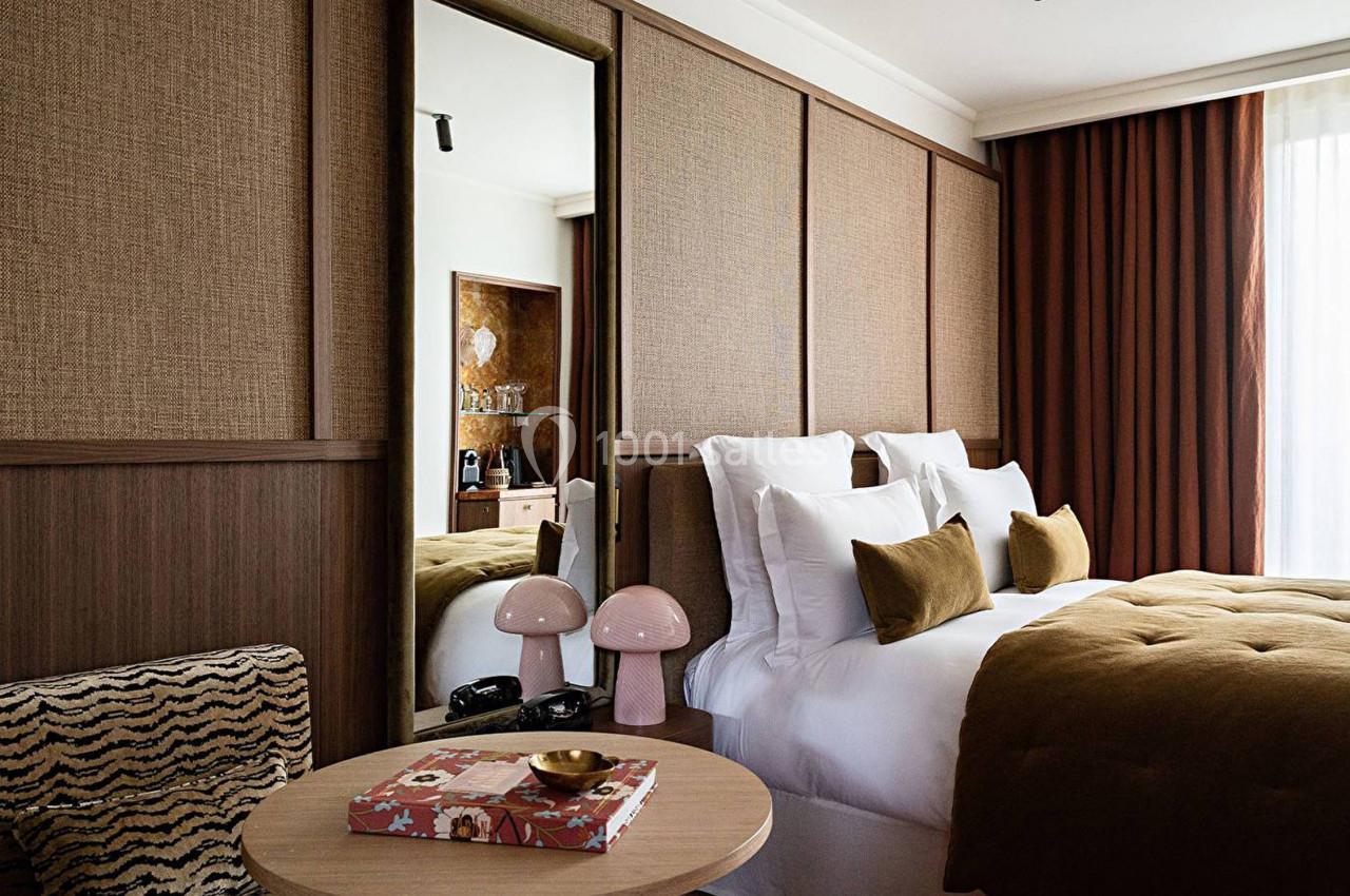 Chambre élégante avec lit double, coussins assortis, miroir vertical, table basse et lumière naturelle filtrée par des…