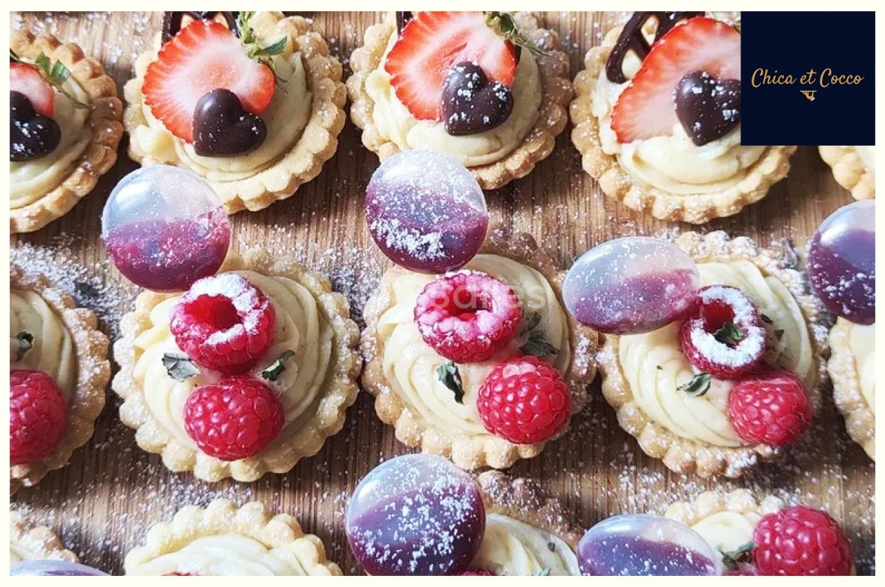 Tartelettes garnies de crème, framboises, fraises, chocolats et décorations colorées, saupoudrées de sucre glace.