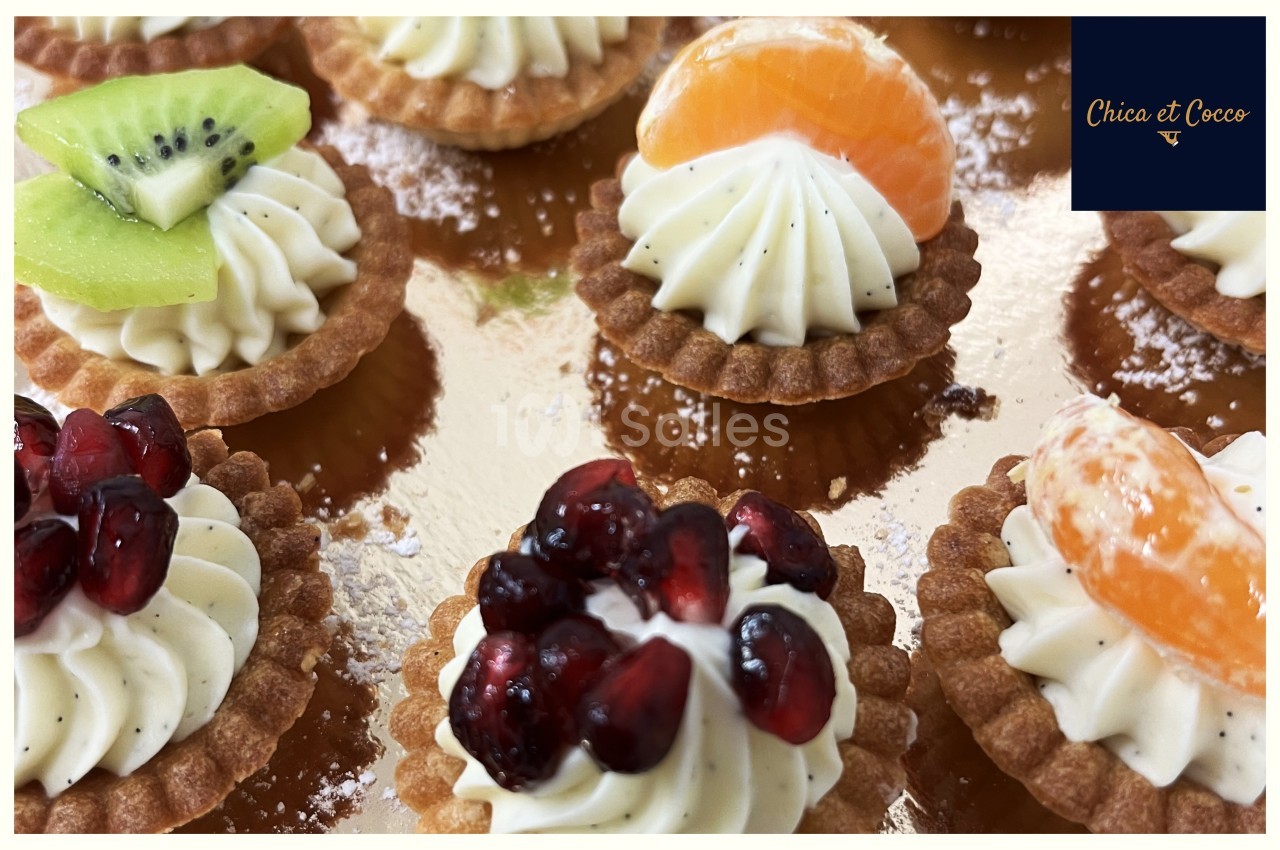 Tartelettes garnies de crème vanillée, décorées de fruits frais comme kiwi, grenade et clémentine, sur un plateau doré.