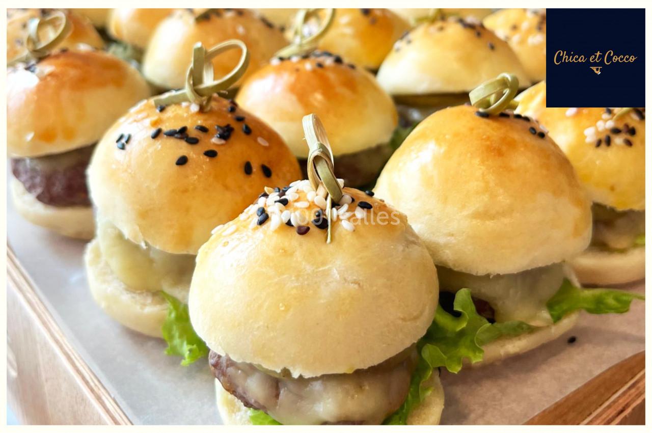 Plateau de mini-burgers garnis de salade, fromage et steak, avec pains dorés et graines de sésame.