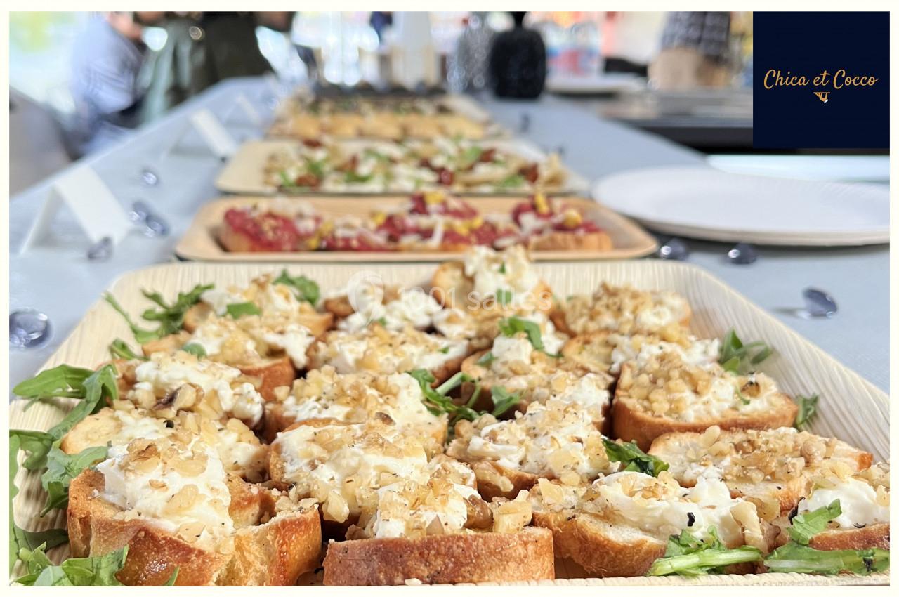 Plateau de toasts garnis de fromage frais, noix concassées et roquette, disposés sur une table de buffet.