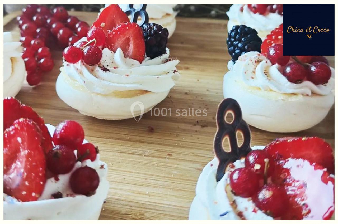 Petites pavlovas garnies de crème chantilly, fraises, groseilles et mûres sur une planche en bois.