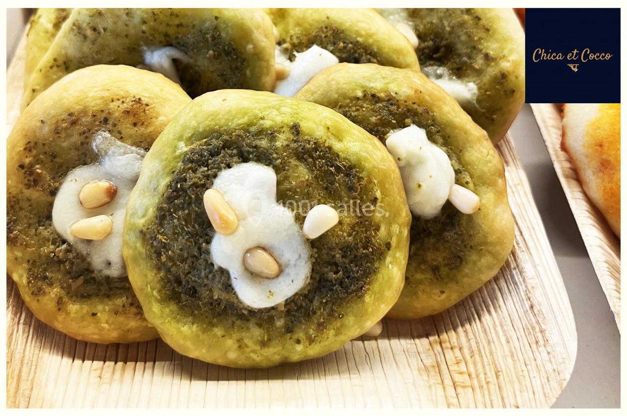 Petites pizzas garnies de pesto, fromage fondant et pignons de pin, présentées sur un plateau en bois.