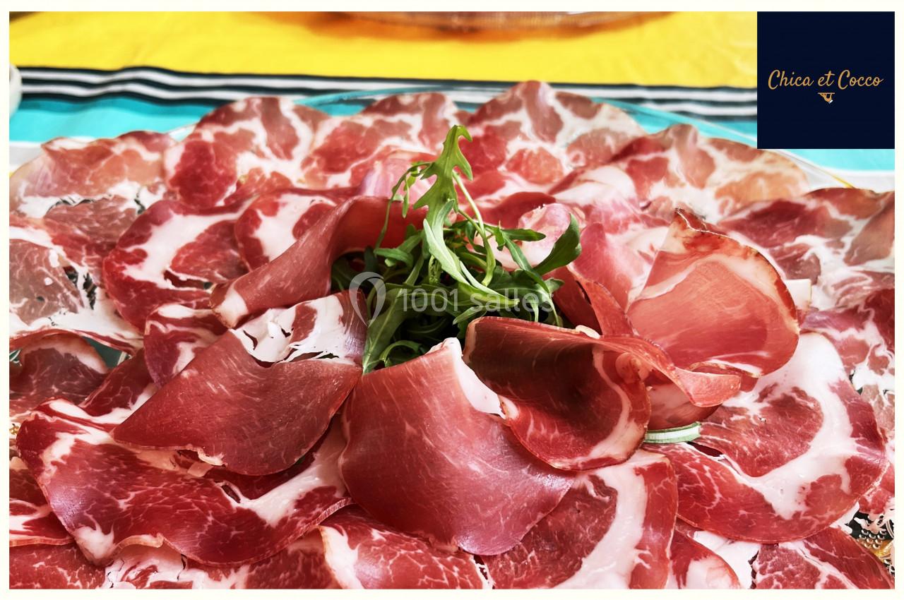 Assiette de charcuterie garnie de tranches de viande séchée et de roquette, présentée sur une table colorée.