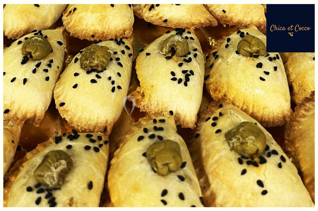 Assortiment de feuilletés dorés garnis d'olives vertes et parsemés de graines de sésame noires.