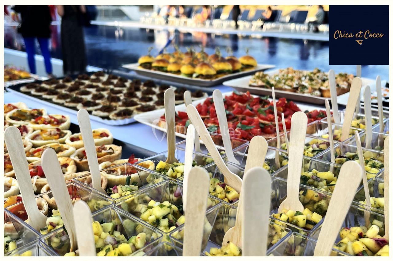 Buffet coloré avec verrines de salade, amuse-bouches variés et mini-burgers disposés près d'une piscine.